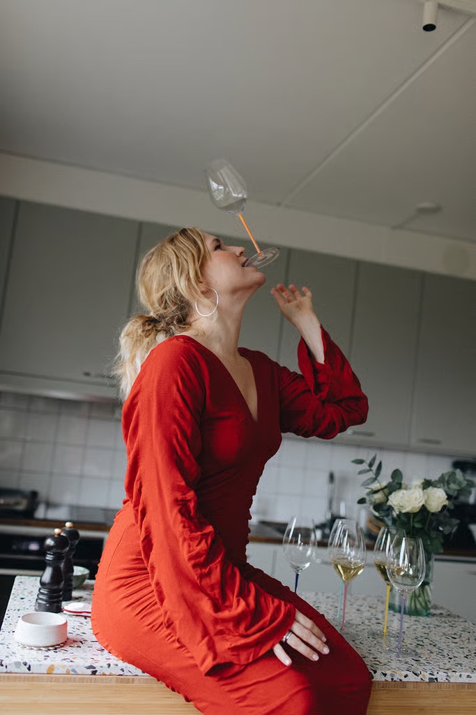 Frida Lund i rött, balanserar ett vinglas i köket. Foto Mira Wickman.